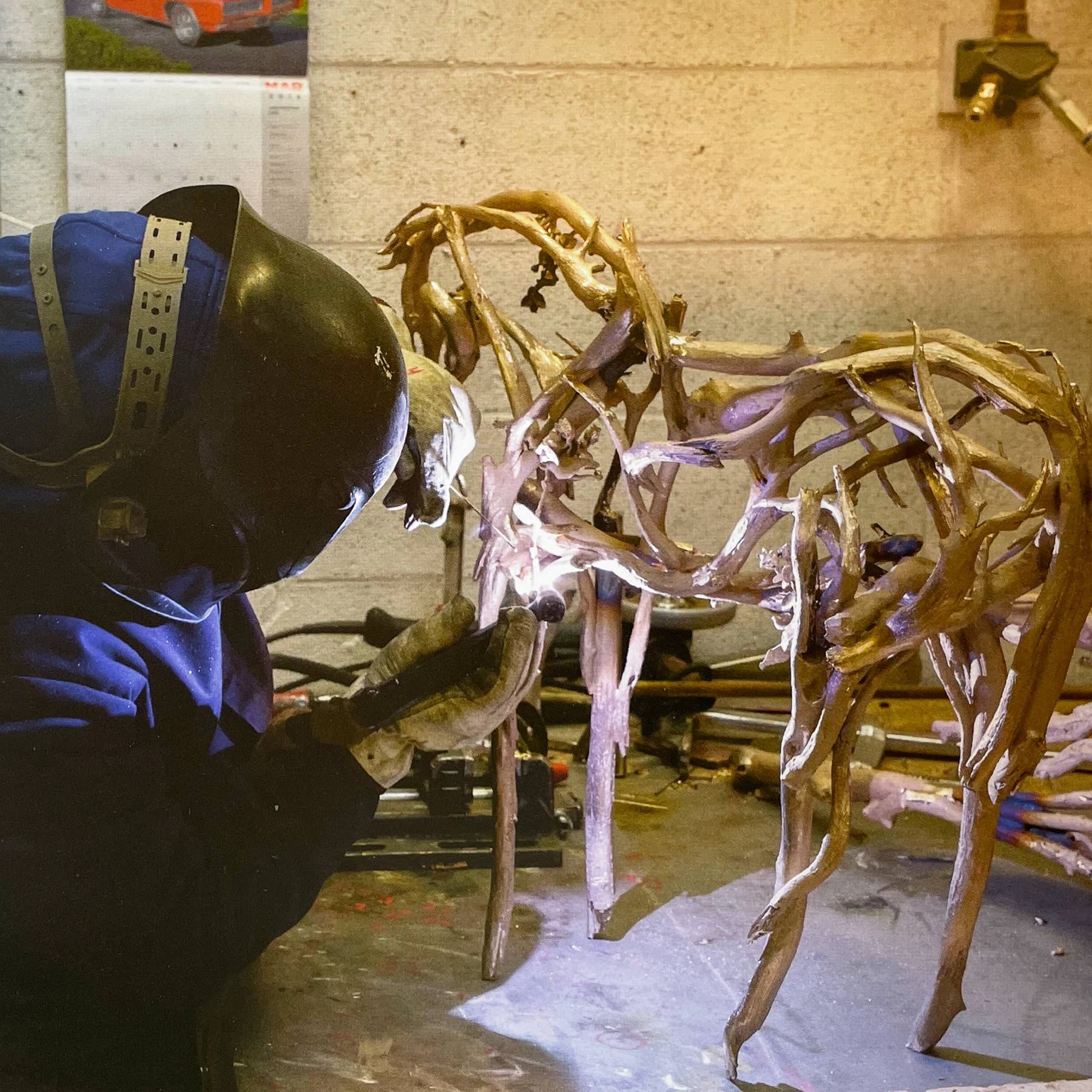 a person in protective gear welding joints of a bronze sculpture together